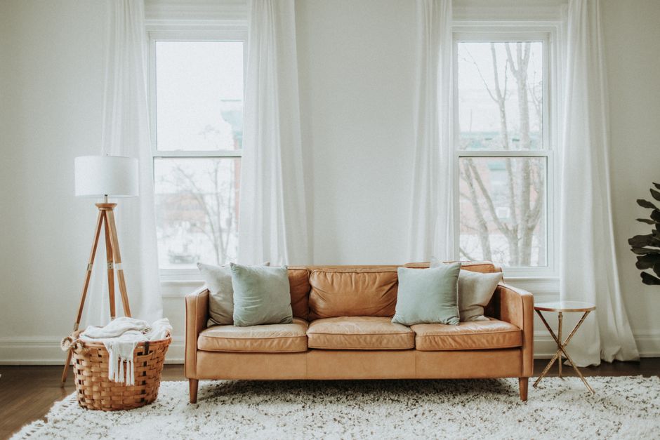 A close-up view of a modern living room featuring a blue fabric sofa with a beige throw blanket draped over the armrest, indicating recent use or cleaning. Next to the sofa is a small, round, black si